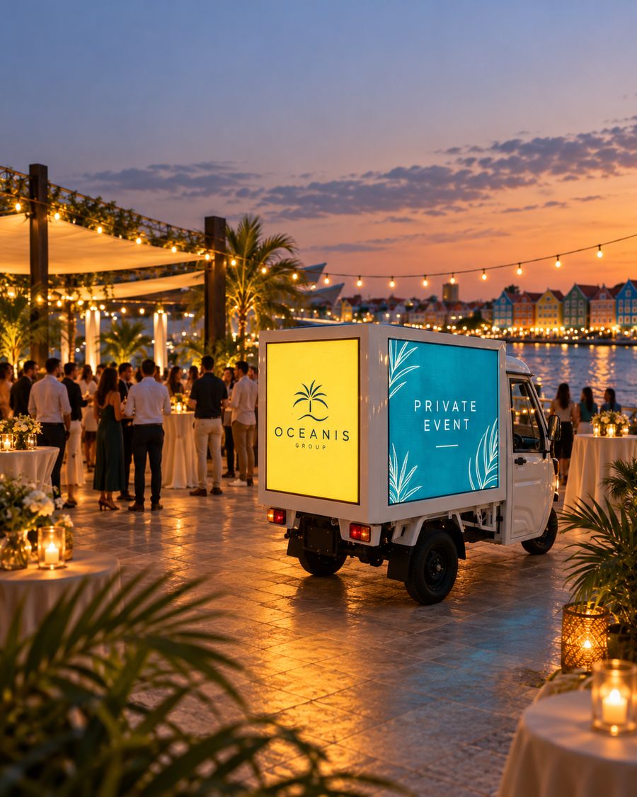 The tuk-tuk at a corporate evening event by the water, a company logo on its screens